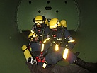 Im Tank kümmert sich der Rettungstrupp um den verunglückten Helfer und schließt ihn an die eigene Druckluftflasche an. Quelle: THW/Anja Villwock
