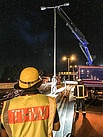 Nachdem die Laterne mit einem Stopp am Ladekran gesichert wurde, trennt ein Feuerwehrmann den Sockel der Laterne mit einem Trennschleifer ab. Quelle: THW/ Florian Knapp
